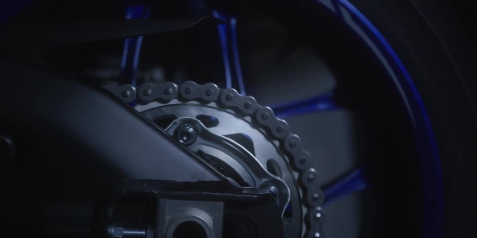 Motorcycle chain and sprocket in closeup with blue rim details in the background