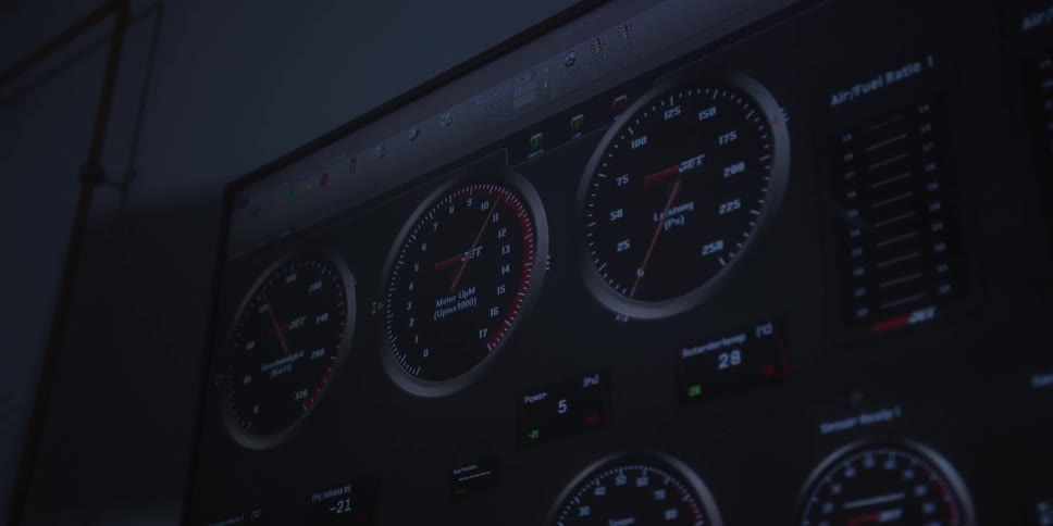 A dimly lit computer monitor displays a dashboard of digital gauges with needles twitching and numbers fluctuating to show realtime performance data