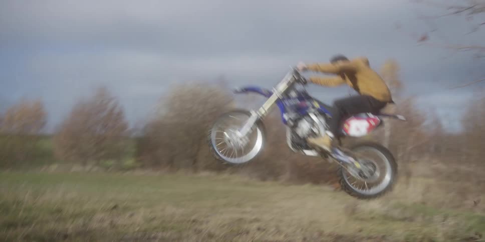 A motorcyclist jumps a dirt bike mid air over a grassy field