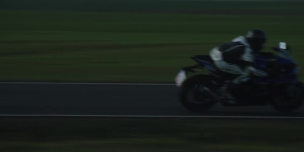 A person in full gear rides a motorcycle at high speed down a rural highway the green countryside blurring past them