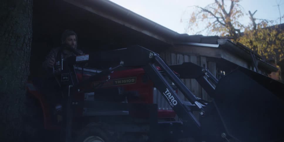 A farmer drives his tractor out of the garage at midday