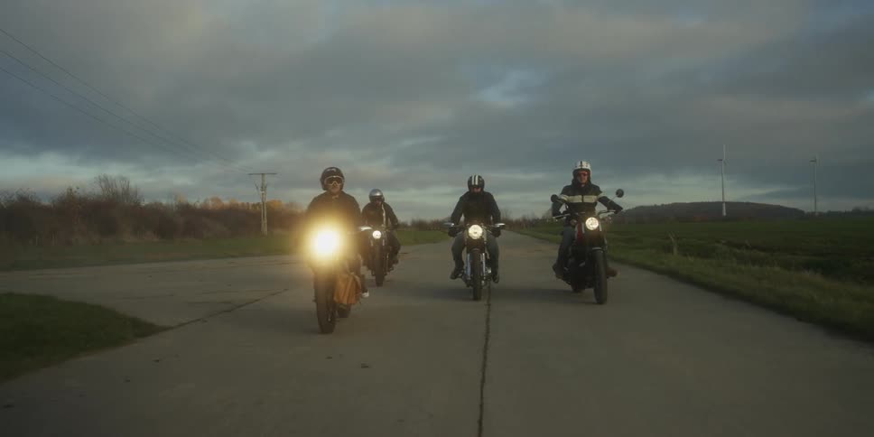 Group of people riding motorcycles on a rural road with a wind farm in the distance