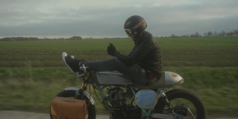 Man riding a motorcycle on a rural road with his feet on the handlebars