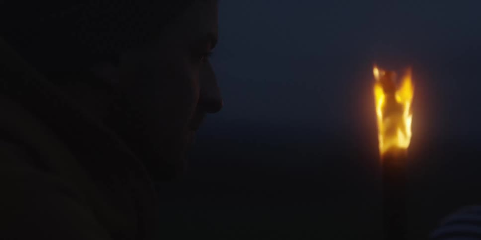 Man looks at a lit torch in a dark setting