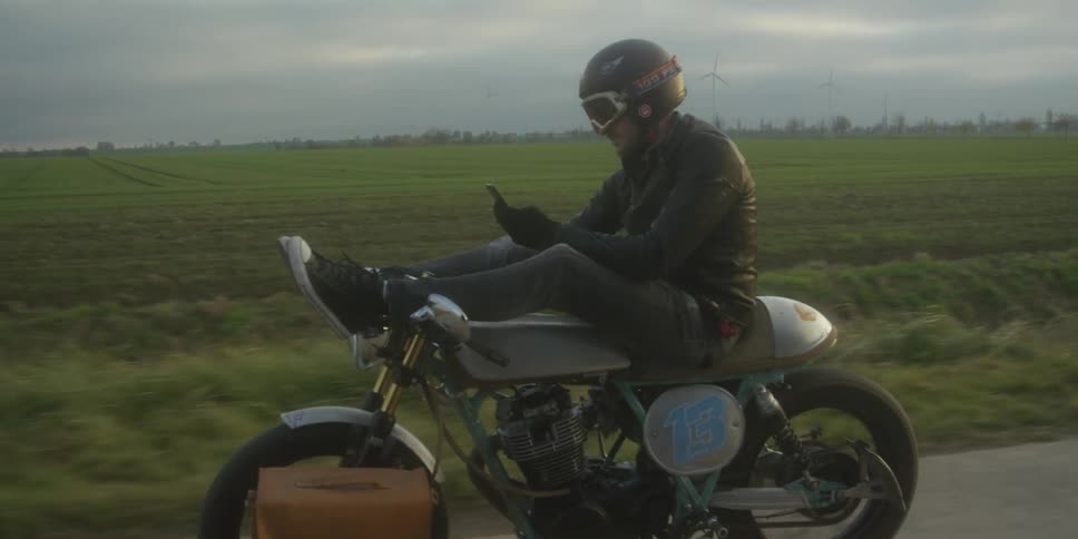 A man rides a motorcycle with his feet up while looking at his phone on a rural road