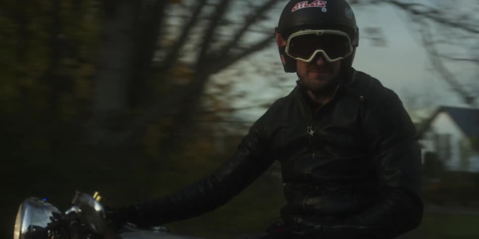 Two men on motorcycles ride on a neighborhood street