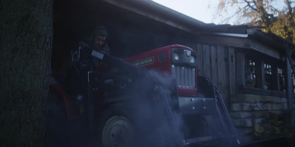 A man preparing to drive an agricultural tractor from a machine shed during daytime
