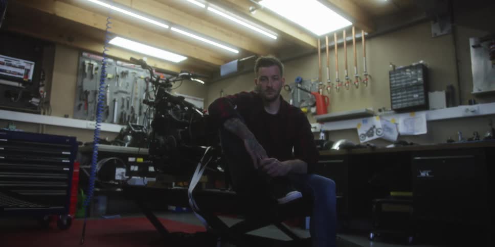 Man sitting on motorcycle lift in workshop equipped with tools and mechanical parts