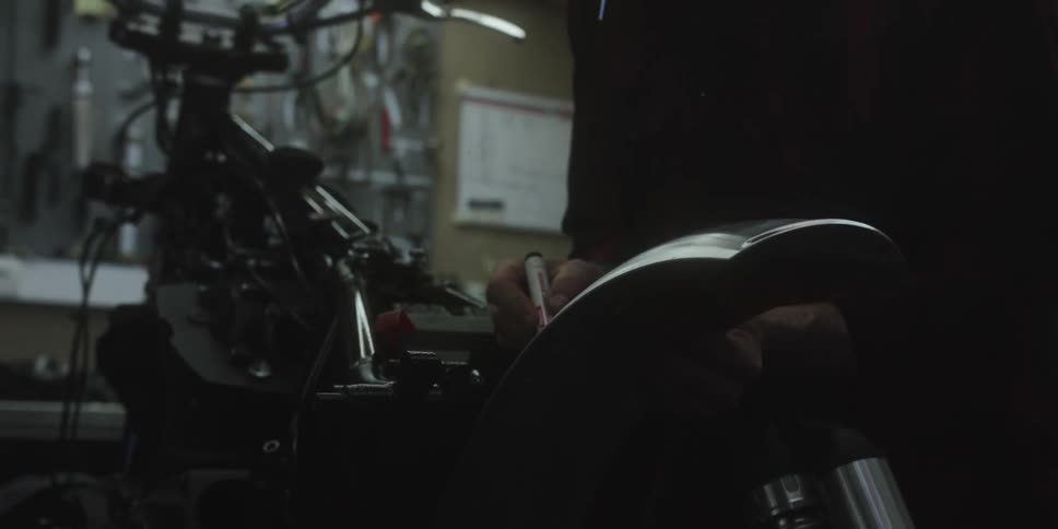 A man works on a motorcycle part inside a dimly lit workshop