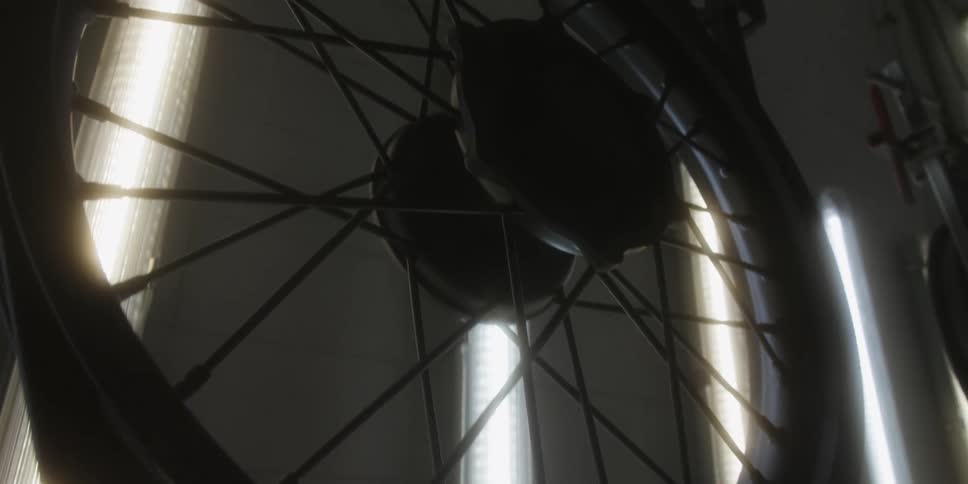 This short video shows a closeup dimly lit shot of a bicycle or motorcycle wheel spinning the wheels spokes and rim are silhouetted against a bright vertically oriented light source in the background which creates a dramatic highcontrast effect