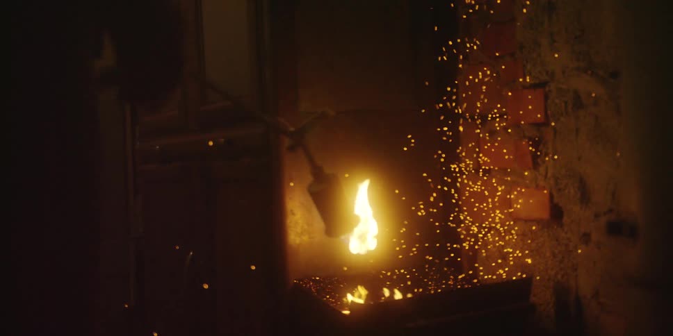 Person sends fire from a torch into a metal drawer while working in a dark room