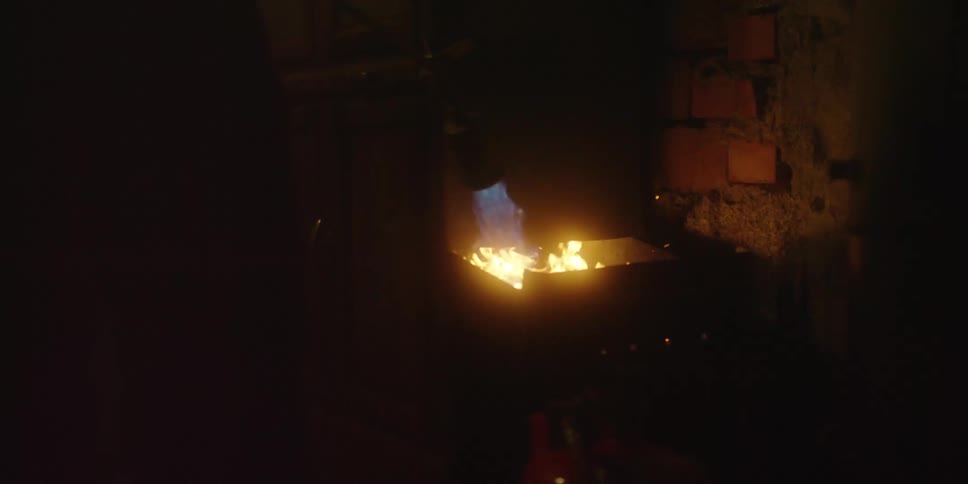 A industrial workspace with heat being applied to metal initially generating a brilliant cascade of orange sparks against a wall which then subsides to reveal a concentrated blue flame on the material