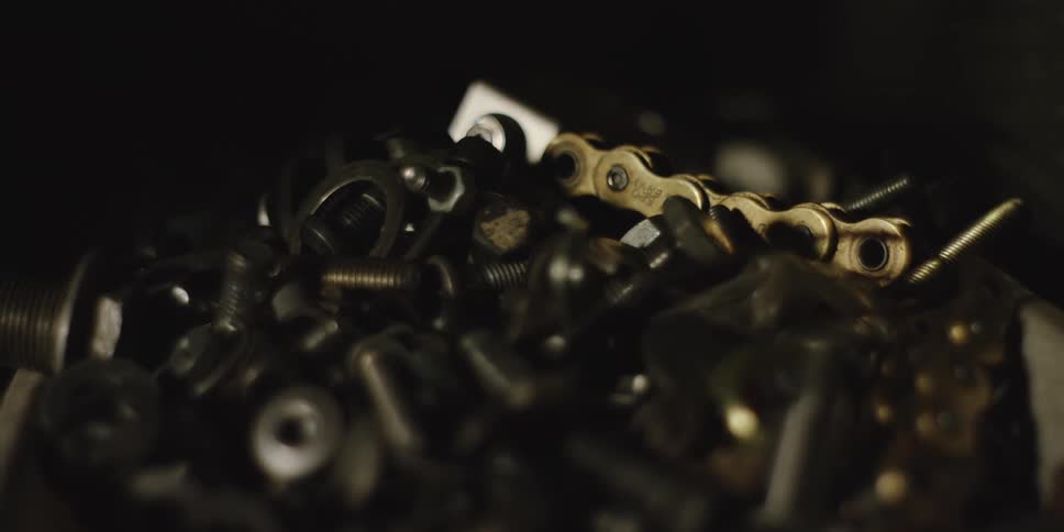 A closeup shot focuses on a dark pile of assorted metal objects including various nuts bolts and washers among the duller hardware a section of shiny goldcolored chain links stands out in the centerright
