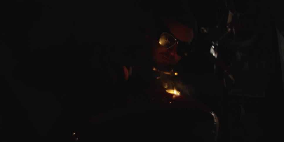 A closeup shot in a dark environment shows a person wearing protective eyewear engaged in a welding process on a red metallic object likely a motorcycle fuel tank which has the word tisha written on it