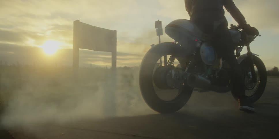 A motorcyclist performs a burnout creating smoke on a paved road at sunset