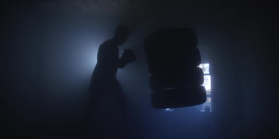 Boxer working out hitting a punching bag in a dark room as sunlight shines through the window