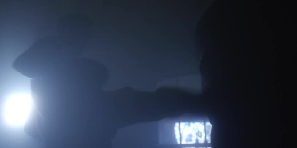 A silhouetted boxer trains with intensity in a dark smokefilled room relentlessly striking a heavy bag illuminated by a dramatic backlight