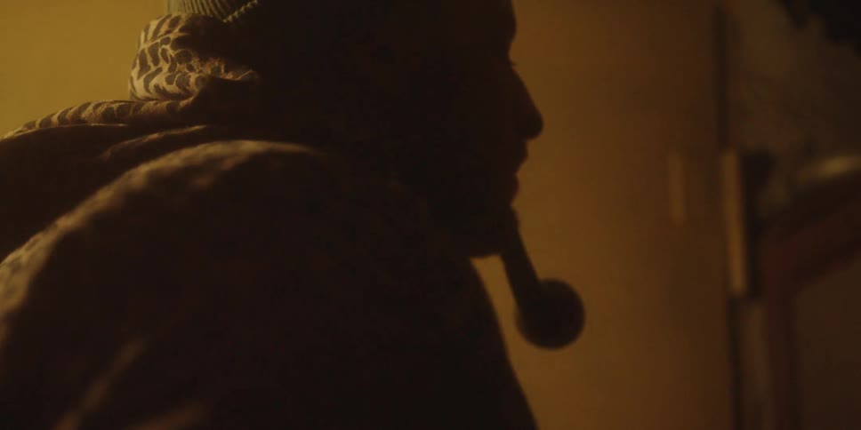 A man lights his pipe before carrying a rack full of hanging meats