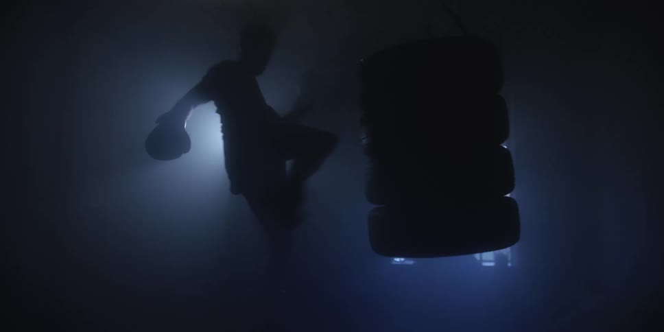Person trains with punching bag in dark setting filled with mist and backlight