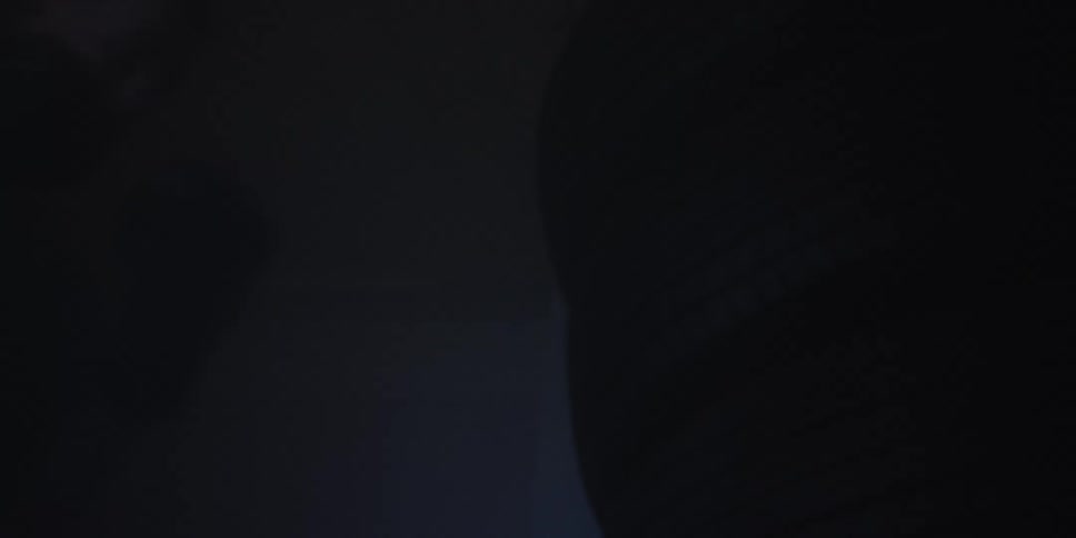 A deeply shadowed lowkey view where the right side is dominated by a male who is boxing using a hanging tire boxing bag