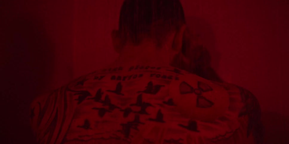 This video shows a closeup of a persons back which is heavily tattooed under a deep red light the tattoos include flying birds mountains what appears to be a camera on a tripod and a nuclear symbol