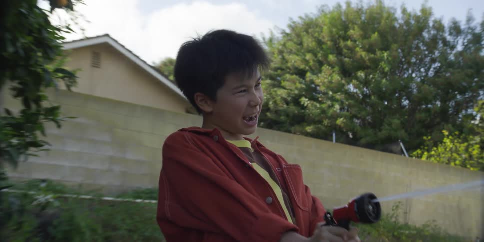 The boy is spraying a hose in his yard