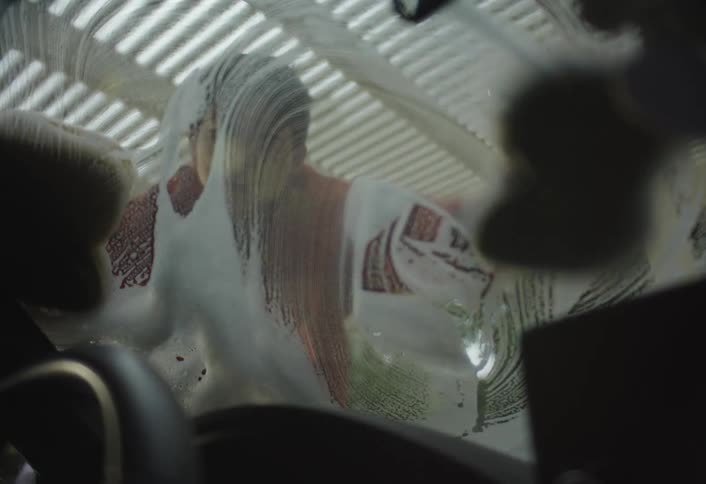 Person cleaning windshield with sponge viewed from inside car