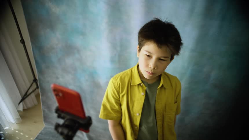 A boy smiles and makes playful faces while recording himself on a smartphone in a studio