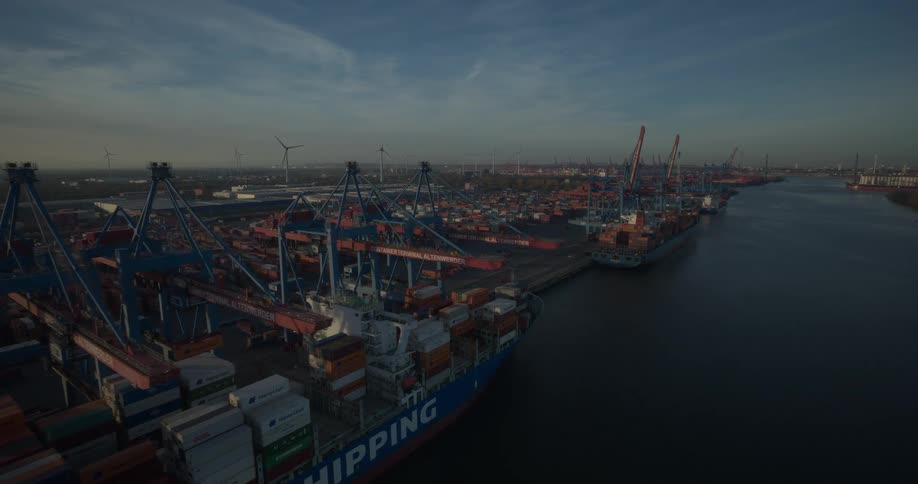 Aerial view of a large shipping port with a cargo ship and container stacks along a wide river