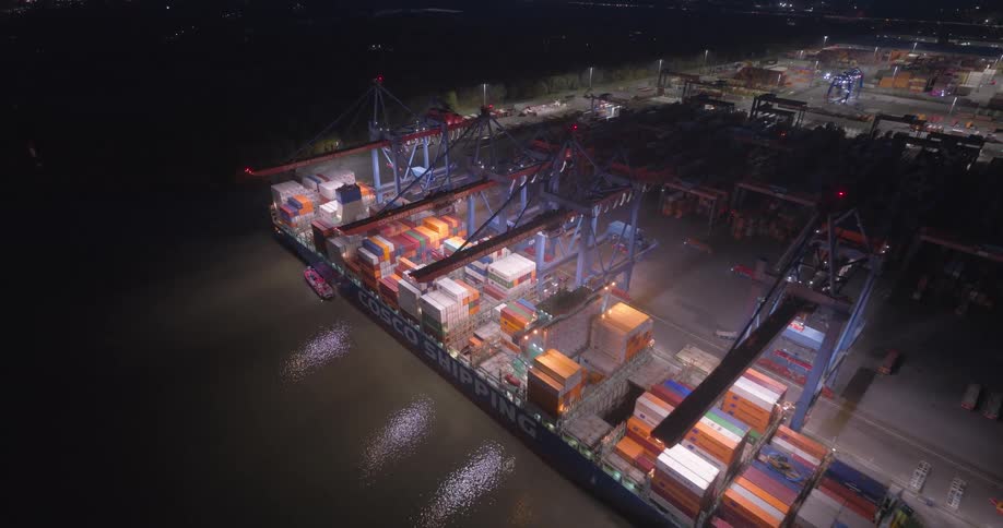 Cargo vessel docked at night port with cranes operating illuminated containers