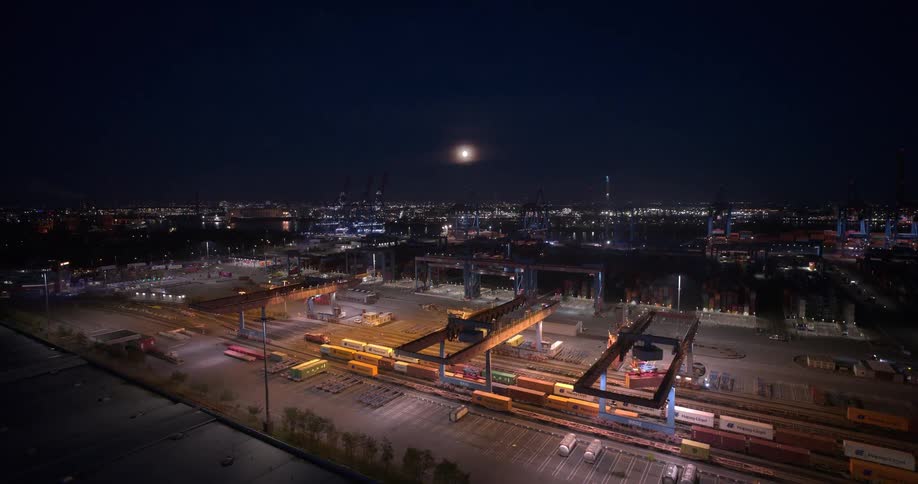 Aerial view of a illuminated shipping yard with trains and containers under a dark sky
