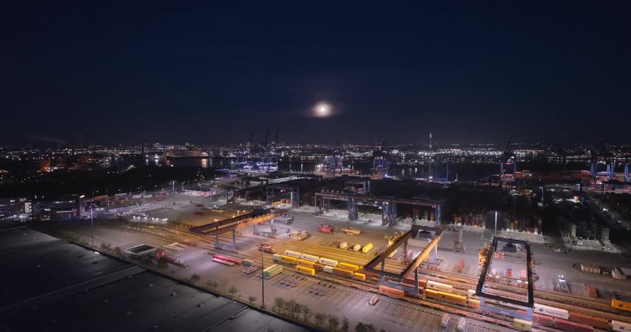 Industrial complex lit at night with a full moon over the city