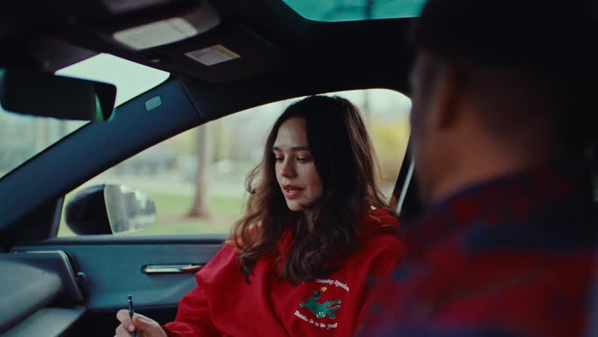 The woman talks with a man in the car while writing