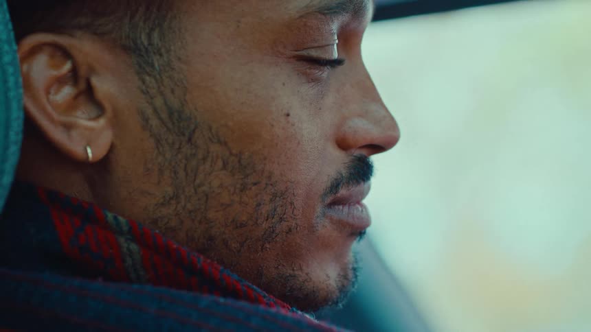 A close view of a man with a beard and an earring looking intently out a car window wearing a patterned scarf