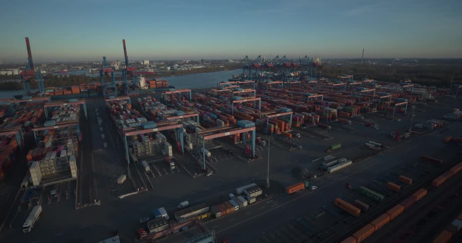 A seaport filled with stacked containers as a series of trucks move in and out carrying loads at sunset