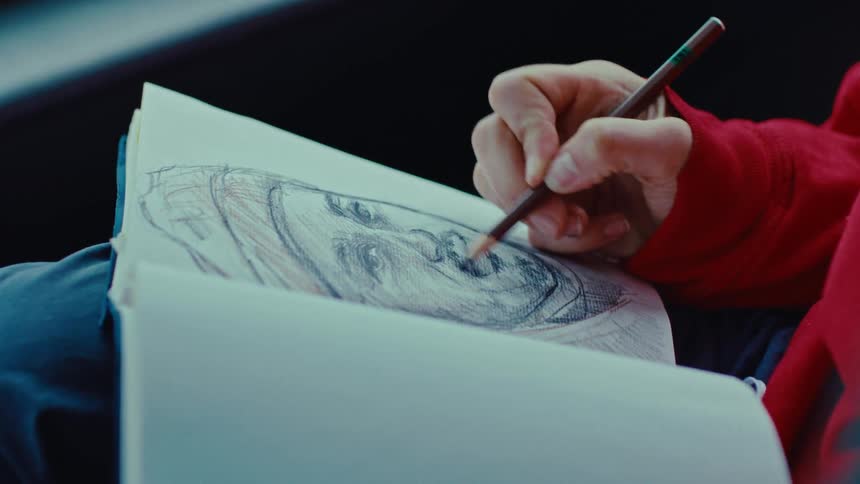 Female hands sketching a portrait of a male face on a sketchbook indoors during day time