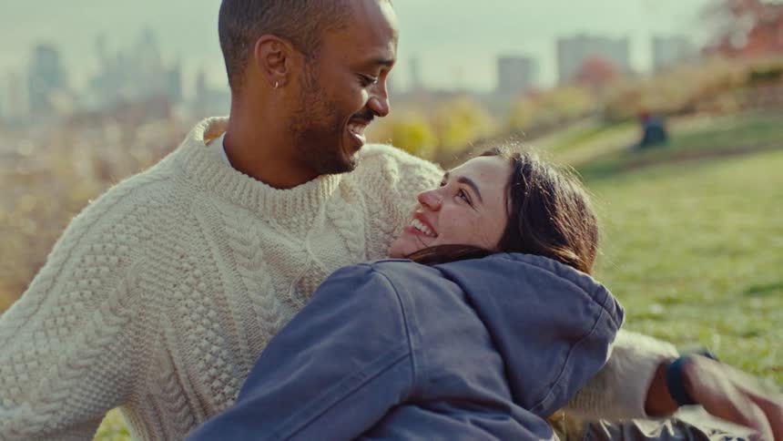 Man holding a woman lying down while touching his face to hers in a park