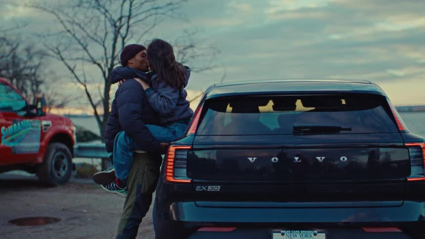 Man standing next to his car holding his girlfriend as they hug and kiss