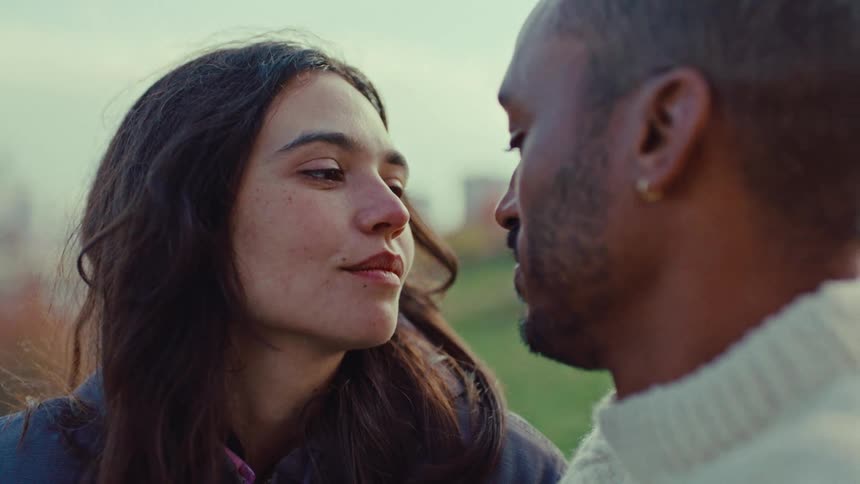 A young woman gazes lovingly at her partner as he gently strokes her hair during an intimate moment outdoors