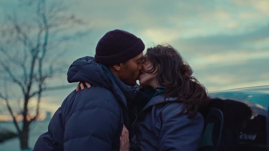 Close up of a young couple kissing each other romantically while standing beside their vehicle outdoors at sunset
