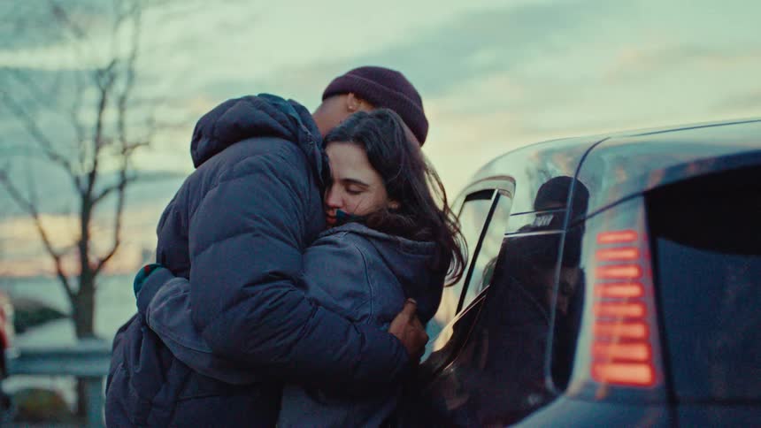 A couple wearing winter jackets embraces tightly beside a parked car