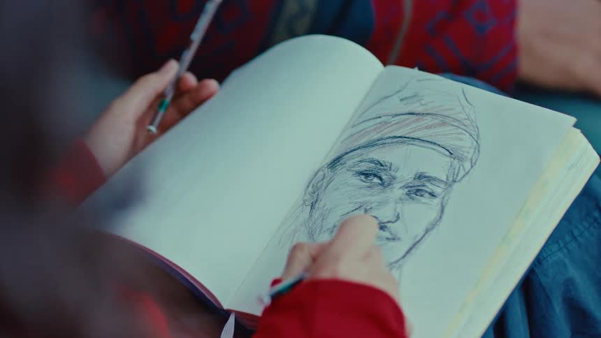 Person sketching portrait with pencil in notebook