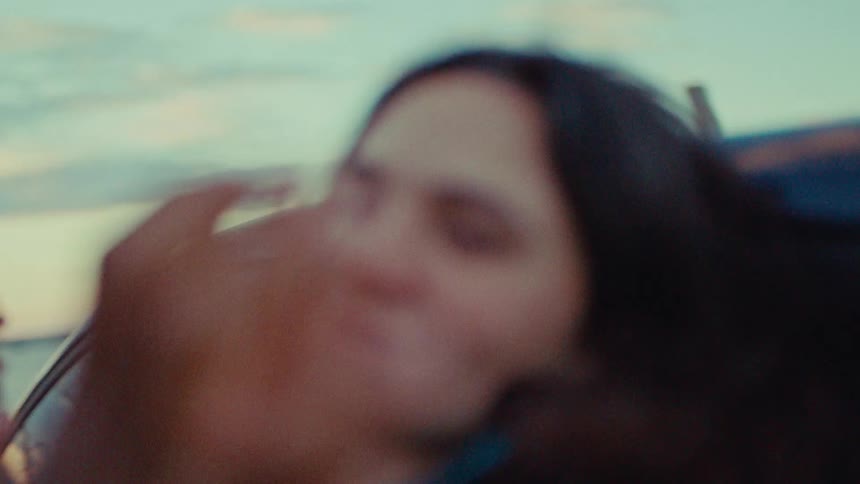 Close up of a young woman holding hands with her male partner while standing outdoors beside a vehicle at sunset