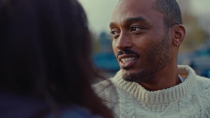 Man in a light sweater talking to someone in front of him outdoors