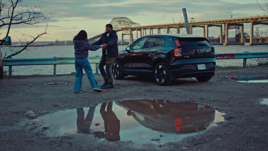 A couple romantically dances beside a parked car near the waterfront at dusk
