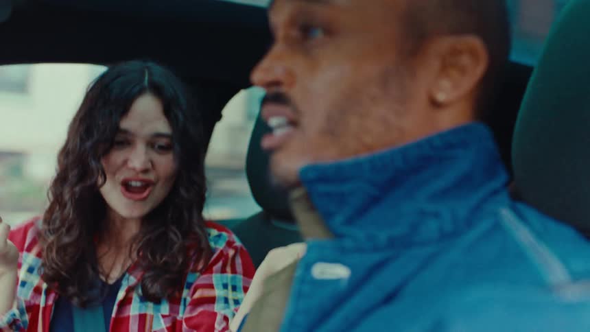 Young adult man driving a car and singing and laughing next to a young adult woman singing too indoors during day time