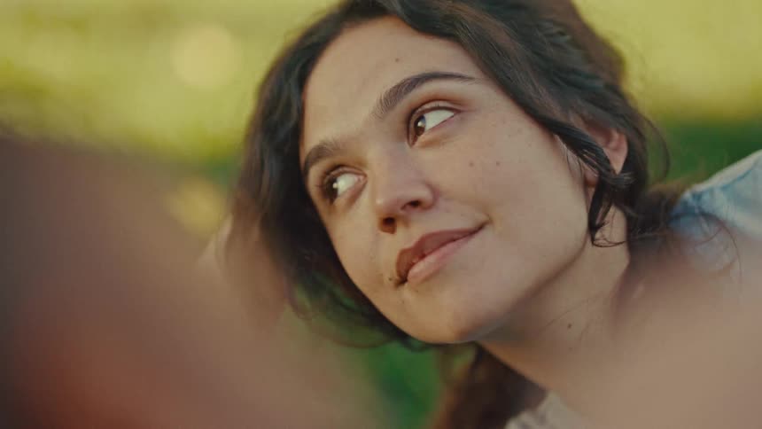 Close up portrait of a young woman conversing while lying on an outdoor field during a picnic date