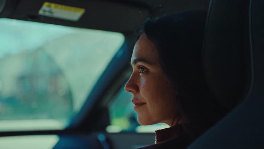 A woman sits in a moving car gazing forward with a calm expression