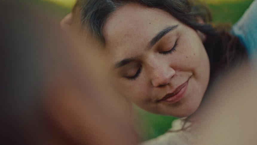 An intimate coseup of a young womans face smiling and looking up as a persons hand in the foreground with head blurred gently caresses her cheek in a moment of warmth set outdoors with soft natural lighting
