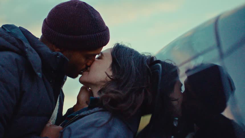 Man kisses the woman leaning against a reflective vehicle on a winter day